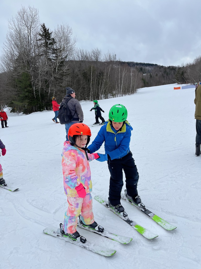 Two children practice skiing, holding each other up for support