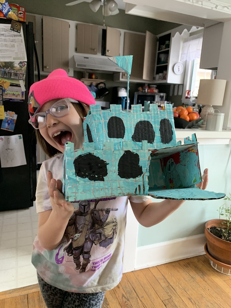 girl in pink hat and glasses holding blue cardboard castle