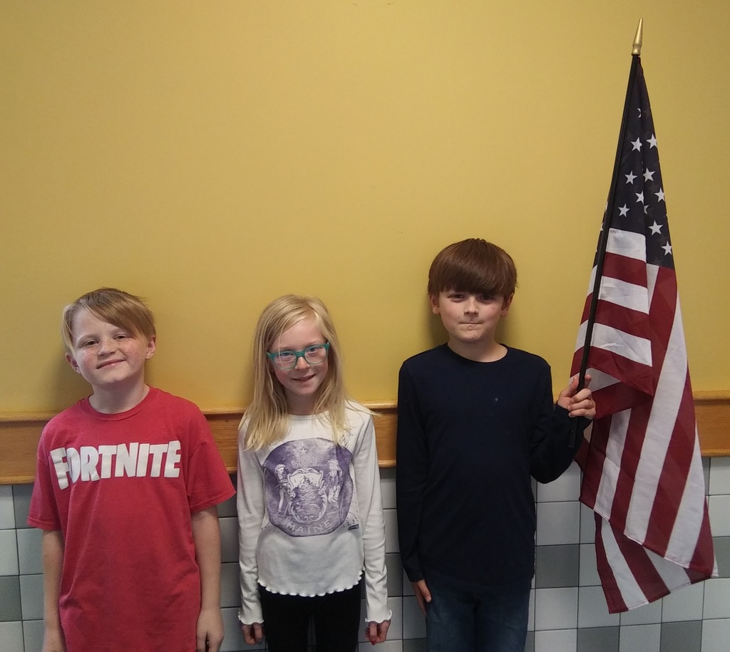 three students standing in yellow hallway holding American flag