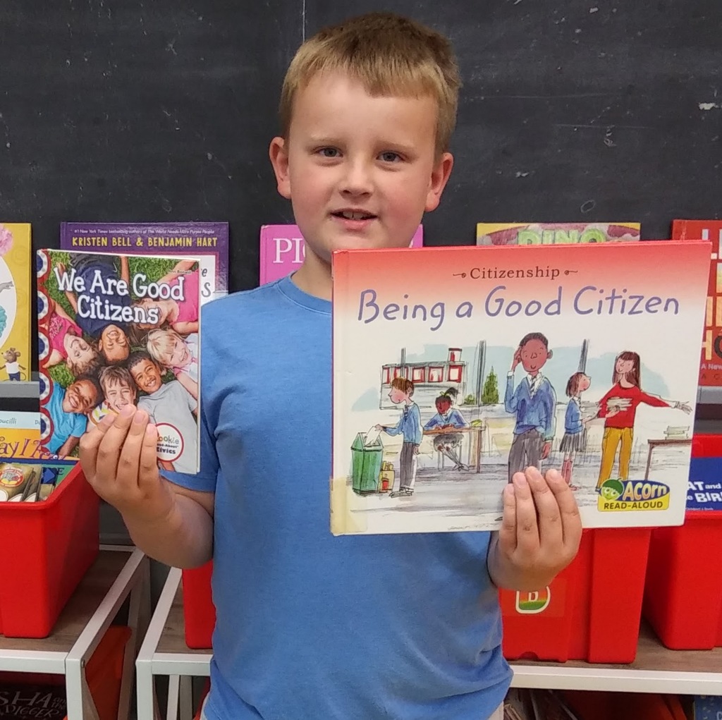 first grade student in blue shirt holding two books about bring a good citizen